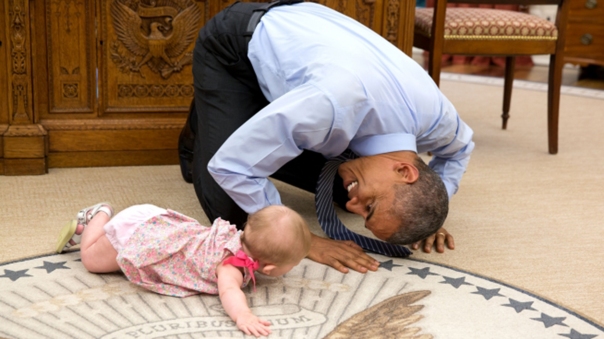Obama on the floor playing with a baby.